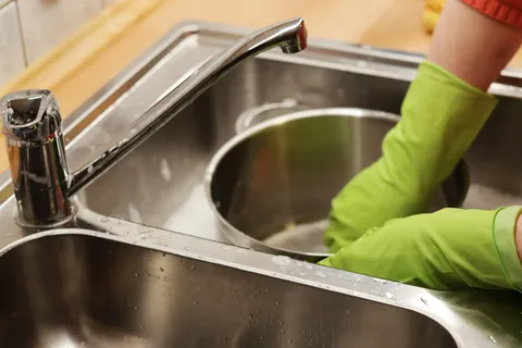 Iemand in een groen shirt wast rvs vaatwerk af