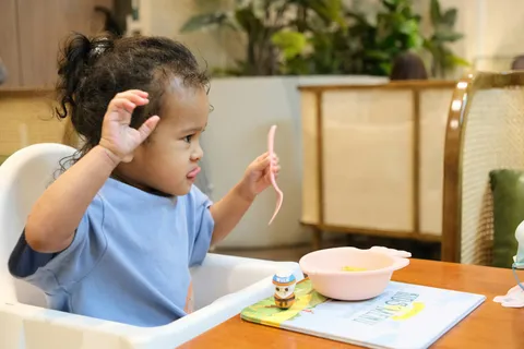 Klein kind in een kinderstoel met een lepel en een kom